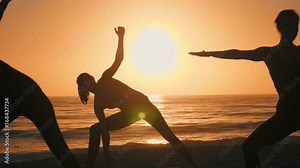 Group of 3 women practicing yoga on the beach against the sunset. Three black silhouettes of their bodies making yoga postures. Sun and the ocean creates ethereal & pure scene