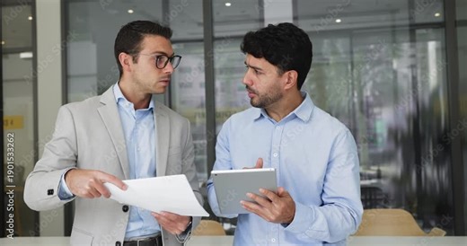 Serious male Hispanic employee asking coworker for advice, using tablet, showing online content to colleague, advisor. Professional expert talking to project manager with gadget, giving consultation