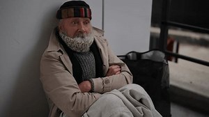 Yawning senior homeless man sleeping peacefully outside in winter, bundled up in warm clothes with bag by side, highlighting social issue of homelessness in urban areas. Shooting in slow motion.