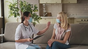 woman doctor help middle aged woman during homecare medical visit with mask on face, female doctor talk with 40s patient give empathy support and prescribes treatment while sitting on sofa at home Stock Video