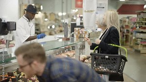 Happy worker on supermarket deli counter serving customers with a smile