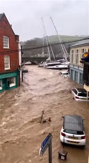 Flash Flood Sweeps Boats into Coastal Village Dartmouth, United Kingdom — March 12, 2025 A sudden flash flood turned the narrow streets of a coastal town into a raging river on Wednesday morning. Torrential rainfall caused a nearby river to burst its banks, sending a surge of brown, debris-filled water through the commercial district and catching residents completely off guard. Dramatic footage captured from a balcony shows the sheer force of the current as multiple yachts and large sailboats we