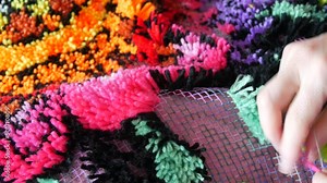 Hand embroidered carpet. A woman using a special hook and thread embroiders a carpet with pink threads. Handmade carpet embroidery. Women's hands create a pattern using multi-colored threads.