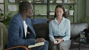 Black male counsellor touching shoulder of frustrated Caucasian female client while comforting her in therapy session