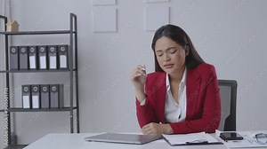 Stressed businesswoman in office shows signs of stress after using laptop, taking a break to relax and ease headache. Office environment with documents and technology