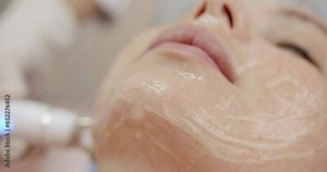 Closeup of professional cosmetologist doing facial microcurrent procedure using modern apparatus for woman client in beauty clinic. Cosmetology and skin care concept