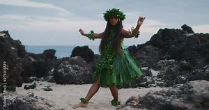 Traditional Hawaiian hula dancing at sunset in slow motion, woman performing Hawaiian hula with haku leis and ti leaf skirt with the ocean in the background