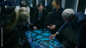High Angle Shot of Team of Government Intelligence Agents Talking while Standing Around Digital Touch Screen Table and Tracking Suspect. Satellite Surveillance Operation in the Monitoring Room.