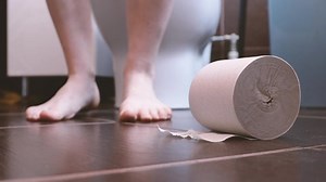 Woman with constipation or diarrhoea sitting on a toilet and holding unrolled toilet paper ready in her hands, close up view of her legs