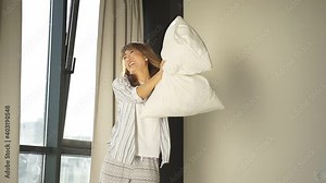 cheerful Japanese woman enjoys the weekend, waking up in the morning a woman in pajamas has fun in the bedroom on the bed, throwing pillows up.
