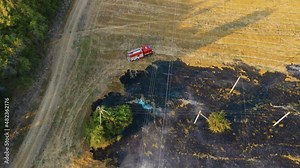 Incident with burning agronomic field after harvesting and red fire truck driving extinguish flame. Emergency case for danger mission and rescue nature saving concept