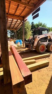 The bulldozer lifts a wooden beam that has undergone various stages of processing and is stored