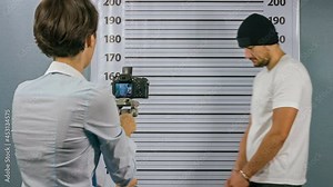 Police woman takes a picture on the camera man who is handcuffed. Mugshot.