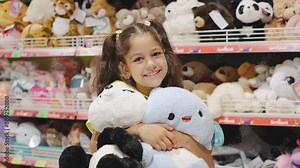 In a store, a young girl is happily smiling while holding plush toys. The shelves are stocked with cute items for kids, radiating joy and innocence, and creating a cheerful ambiance