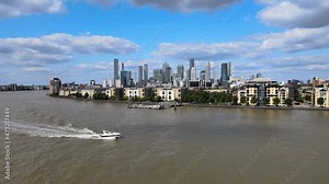 motorboat floating on Thames river. Low houses on bank and tall modern office buildings in distance. London, UK