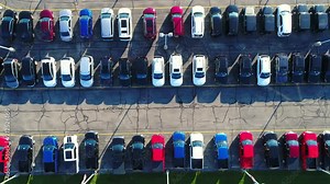 Looking straight down on new car lot, many vehicles for sale, glistening in the sun, aerial view.