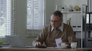 Old man using calculator to calculate personal finance, income, expenses for future plan. Concept of filing tax, tax deduction, tax payment and bill checking.