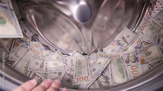 Hand putting USA Dollar banknotes in a washing machine drum. Money laundering concept.