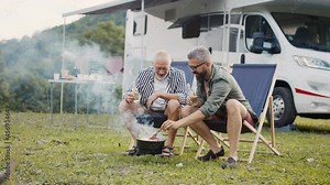 Mature man with senior father talking at campsite outdoors, barbecue on caravan holiday trip.