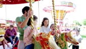 Family riding carousel in amusement park. MS, slow motion.