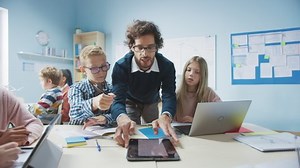 Elementary School Classroom: Enthusiastic Teacher Holding Tablet Computer Explains Lesson to Brilliant Young Children. Kids Learning Programming Languages, Internet Safety and Information Technology