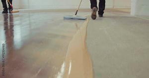 Workers applying a base coat of epoxy resin support using a floor squeegee on the existing concrete surface. Slow motion.