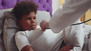 Pediatrician using stethoscope listening to sick little kid at home. Doctor examine ill African-American boy at home. Children medical healthcare concept. Realtime