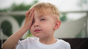 A curious child looks up and out into the distance with a focused expression, as he touches his head