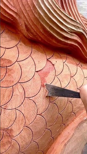 carving detailed fish scale patterns onto a large piece of wood using a sharp metal chisel tool