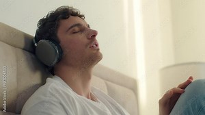 Caucasian man male guy listening music headphones closed eyes enjoyment relaxing sing song gadget technology playlist radio bedroom home satisfaction earphones audio device wireless connection sound