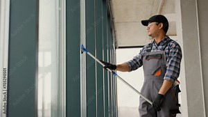 A man in uniform washes a windows with scraper. Professional home or office cleaning service