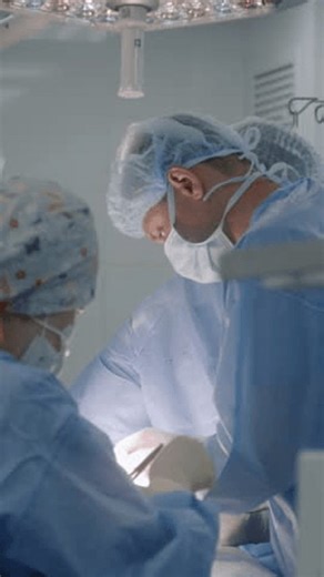 Mature male surgeon in surgical suit with colleagues operate patient in surgery room. Young nurse assists doctors and gives medical instruments. Professional medics stitch wound and finish operation.