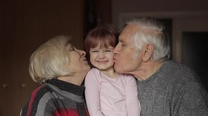 Grandfather and grandmother kissing on cheeks their kid granddaughter at home