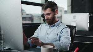 Stupid-looking office employee playing on computer having fun. Portrait of lazy drunk young man in modern office.