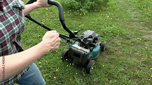Woman gardener starting motor, engine of a lawnmower at the backyard garden, summer work in garden, cutting green grass