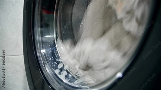 An automatic washing machine washes dirty white clothes. Washing clothes in a domestic washing machine. Close-up video of the spinning drum of a washing machine.