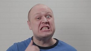A bald man runs a finger along his neck and is angry at the camera. Portrait of a bald man.