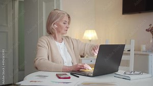 An old lady works on a laptop and then looks at the time on a smart watch