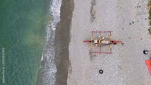 Traditional Filipino banka boat rests on a pebbled beach by calm turquoise waters from above