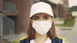 Portrait of the Beautiful Caucasian Lady Courier in Protective Mask Standing Near the Building. Fast Safe Delivery. Postal Girl Home Delivery. Woman Worker Delivery While Pandemic. Close Up