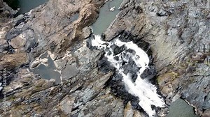 Aerial - Bird's eye view of waterfall tumbling down rock face to create rock pools