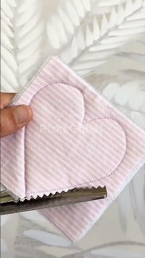 cutting striped pink fabric with zigzag pinking shears following a stitched heart pattern shape