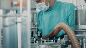 4K A masked technician is servicing the device. Worker repairing a machine. Automatic capsule filling machine, capsule filling device. Production line at a pharmaceutical company. Close up, DOF