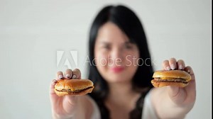 Adult woman shows tasty hamburgers ordered from fast food restaurant. Black-haired lady enjoys eating temptating junk food focus on burgers