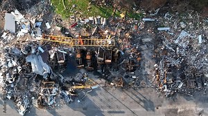 Top down aerial shot of rubble and debris after building fire and explosion. Aerial truck shot of destroyed heavy equipment at municipal building in USA.