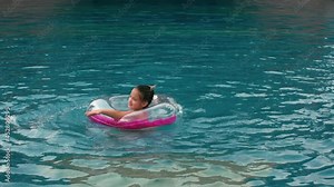 The little cute girl have fun in the swim pool. The child enjoy summer vacation in a swimming pool jumping, spinning, splash water. Slow motion. Happy childhood.