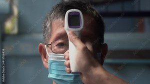 Covid -19 Body temperature measuring for coronavirus. Measures a senior Asian male’s temperature using a non-contact infrared thermometer.