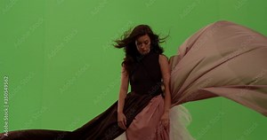 Beautiful woman looks up intently as her dress blows in the wind surrounding her against green screen
