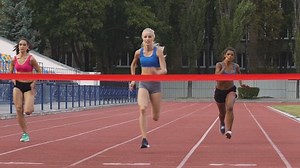 Female marathon runners crossing finishing line on professional sports arena. Fitness women racing competition at stadium, victory celebration, achievement. Motivated blond girl winning speed contest