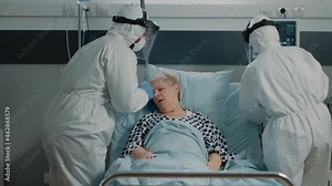 Team of paramedics in hazmat suits helping sick patient with respiratory problem because of coronavirus symptoms. Doctor and nurse using oxygen tube for woman during pandemic lockdown